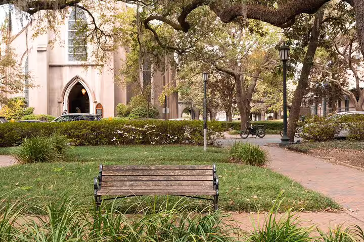 Historic church and park bench in Savannah's haunted square with Spanish moss-draped oak trees