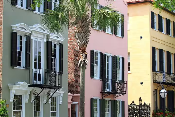 Colorful historic rowhouses with black shutters and wrought iron balconies along a Southern waterfront street