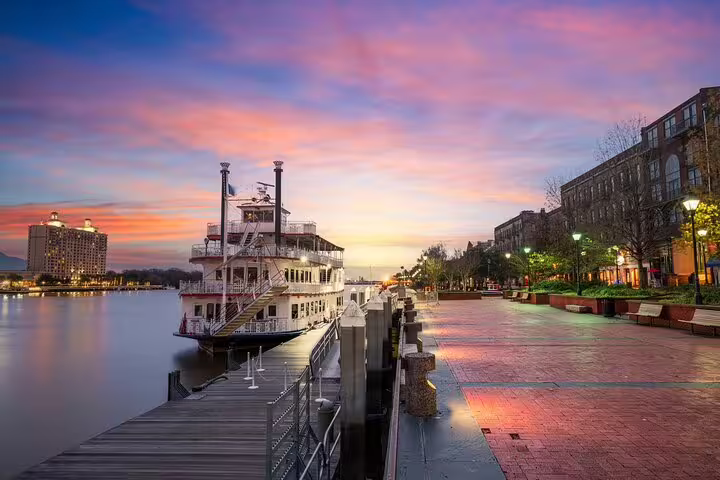 Savannah Waterfront riverboat docked at sunset with glowing city lights and colorful sky