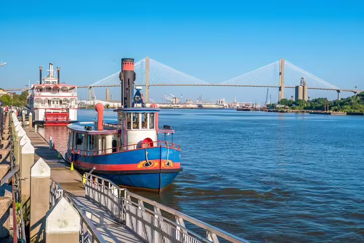 Colorful riverboat and steamboat docked along Savannah waterfront with cable-stayed bridge in background