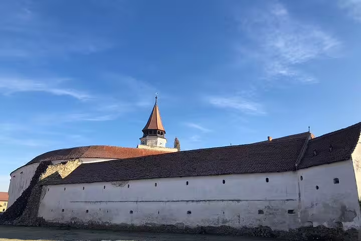 Medieval Saxon fortification wall with defensive tower and pointed spire under blue sky in Transylvania