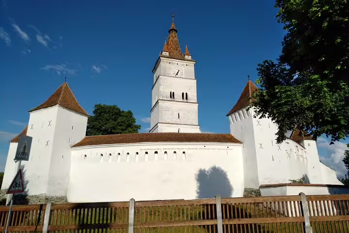 White fortified Saxon church with clock tower and corner bastions under blue sky in Transylvania