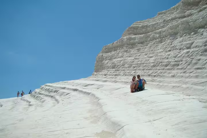Visitors relaxing on the white limestone cliffs of Scala dei Turchi under a bright blue Sicilian sky near Agrigento