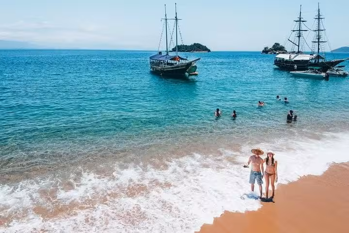 Scenic beach view with anchored sailboats and a couple enjoying the sun, ideal for a relaxing boat tour getaway.