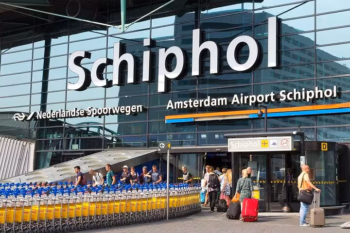 Schiphol arrivals entrance with travelers and luggage carts, meet-and-greet transfer to Maastricht