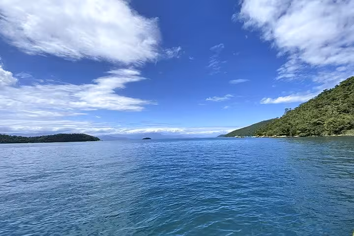 Scenic view of Paraty's serene blue waters and lush greenery under a bright sky, perfect for kayaking adventures.