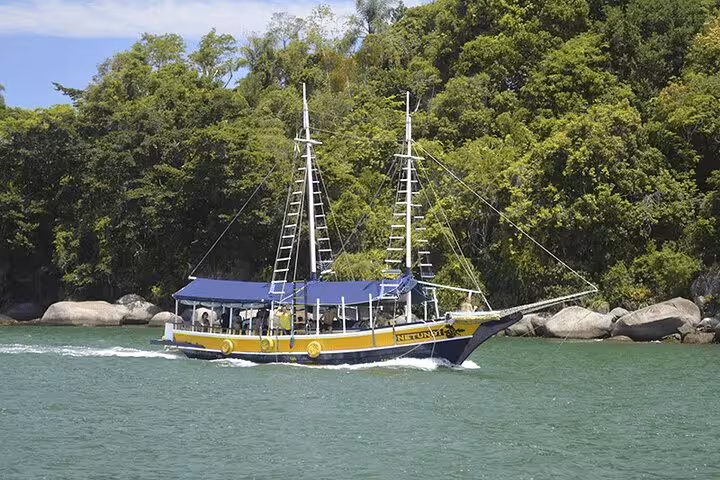 Schooner cruising through lush coastline waters, offering standup paddle and kayak services for a scenic adventure.