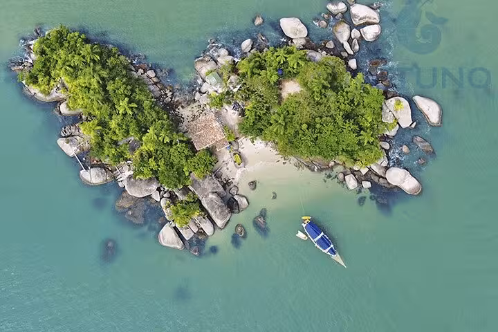Overhead shot of a small, verdant island with a schooner anchored for paddle and kayak services in clear waters.