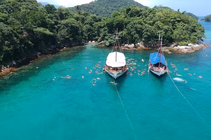 Tourists swimming near anchored schooners in vibrant turquoise waters of Ilha Grande.