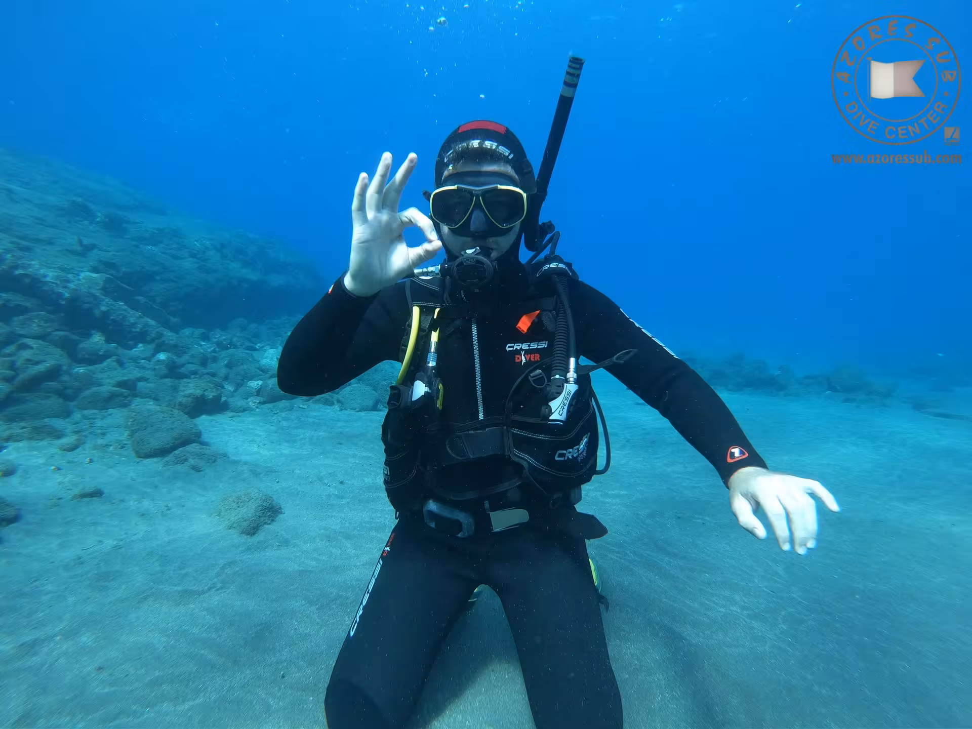 Scuba diver underwater giving OK sign during Baptism at Sea beginner dive experience in clear blue ocean