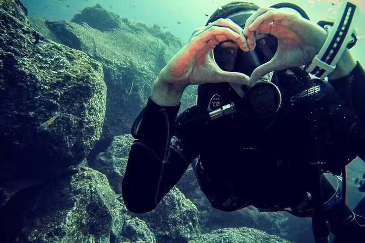 Scuba diver making a heart gesture underwater near rocky seabed during Try Scuba Diving Experience in Funchal, Madeira.