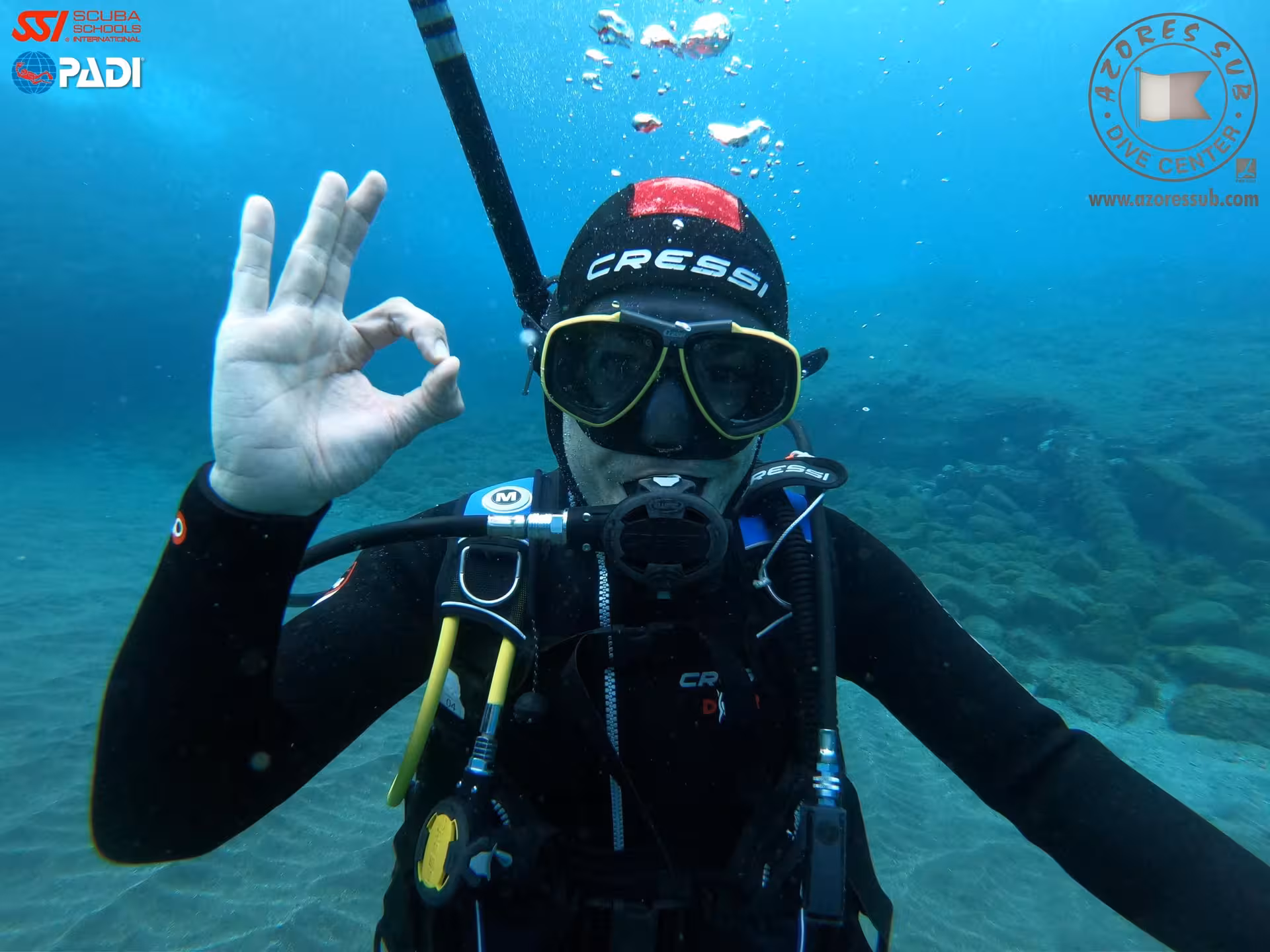 Scuba diver giving OK sign underwater in the Azores, a safe PADI guided dive experience over clear volcanic seabed