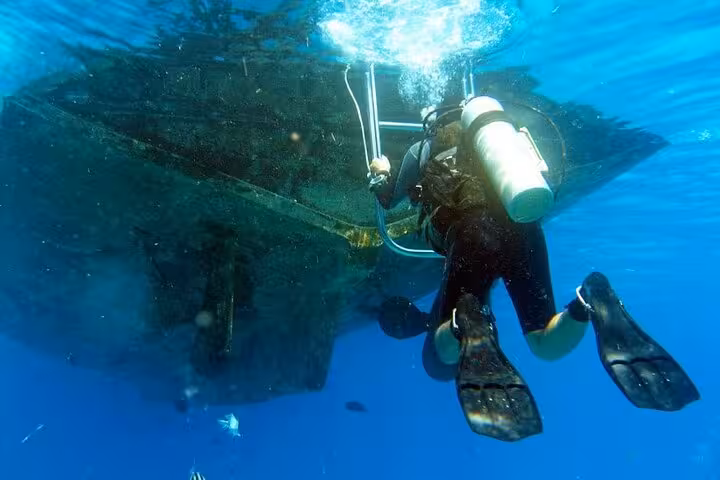 Scuba diver descends beside a wreck in the crystal-clear Red Sea, Egypt, on an underwater diving tour