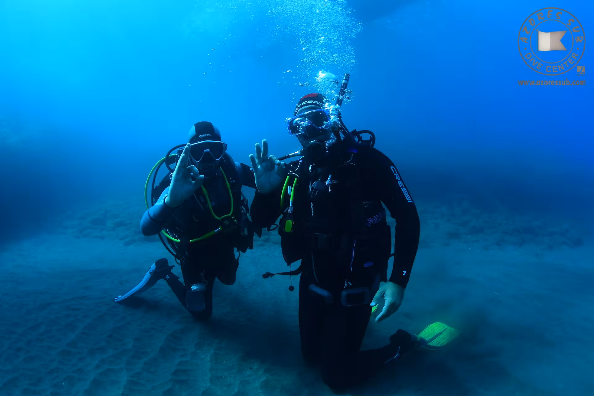 Two scuba divers signal OK underwater during Refresh Dive, guided skills review in calm, clear blue sea
