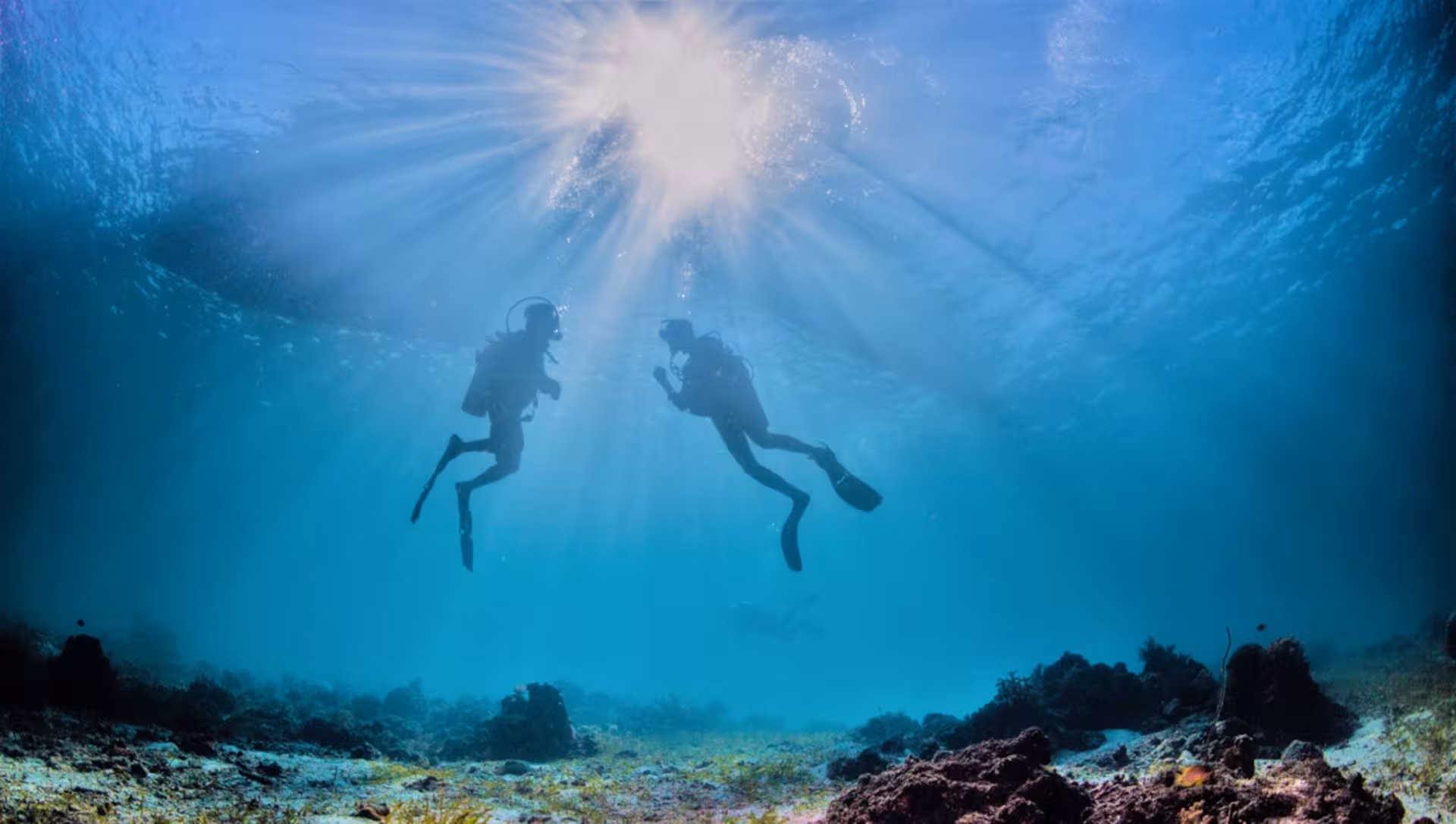 Two scuba divers explore the vibrant underwater world at Ruja Island during a sea baptism experience from San Teodoro.