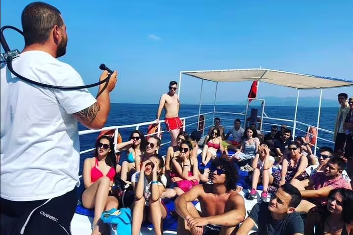 Group of tourists receiving a briefing on a boat deck before a scuba diving tour from Kusadasi, enjoying sunny weather.