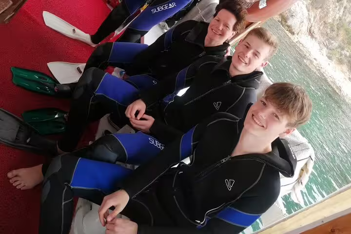 Group of smiling divers in wetsuits on a boat, ready for a scuba adventure from Kusadasi's scenic coastline.