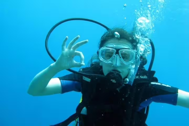 Diver gives an okay sign while exploring vibrant underwater life on a scuba diving tour from Kusadasi.