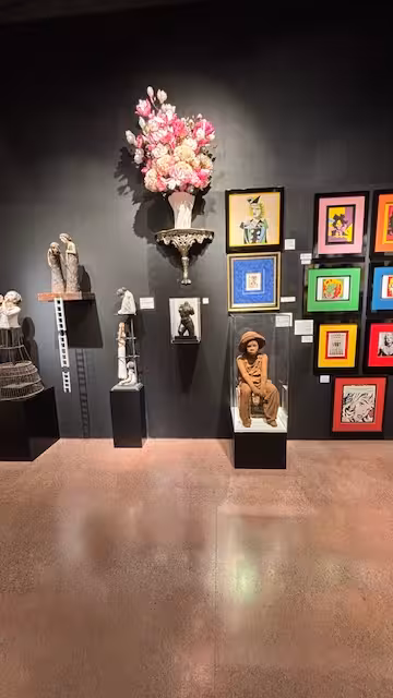 Gallery display featuring diverse sculptures, colorful framed art, and striking floral arrangements for art tour.