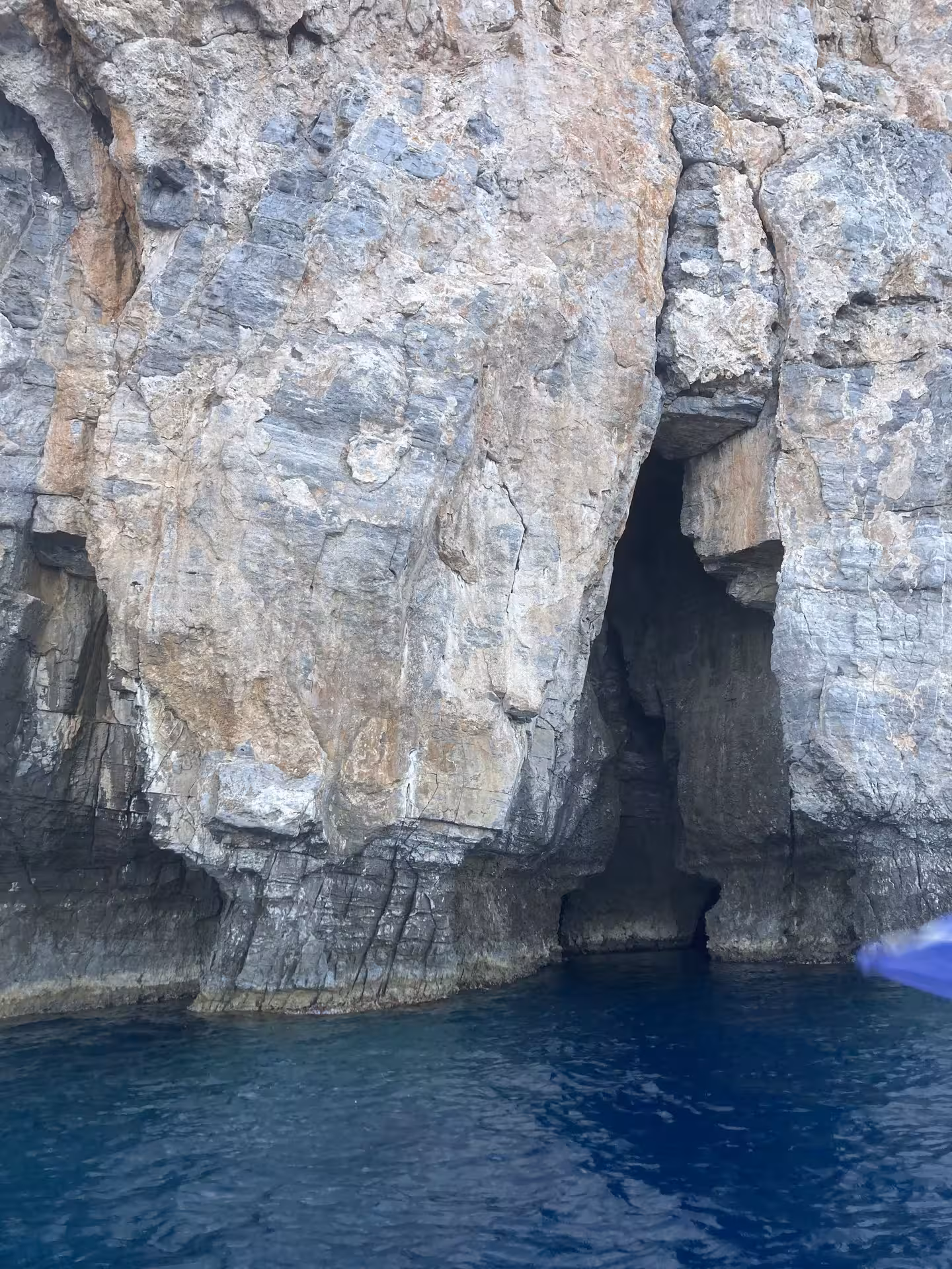 Sea cave entrance in rugged limestone cliffs above deep blue water on Bayliner M17 cave and snorkelling trip
