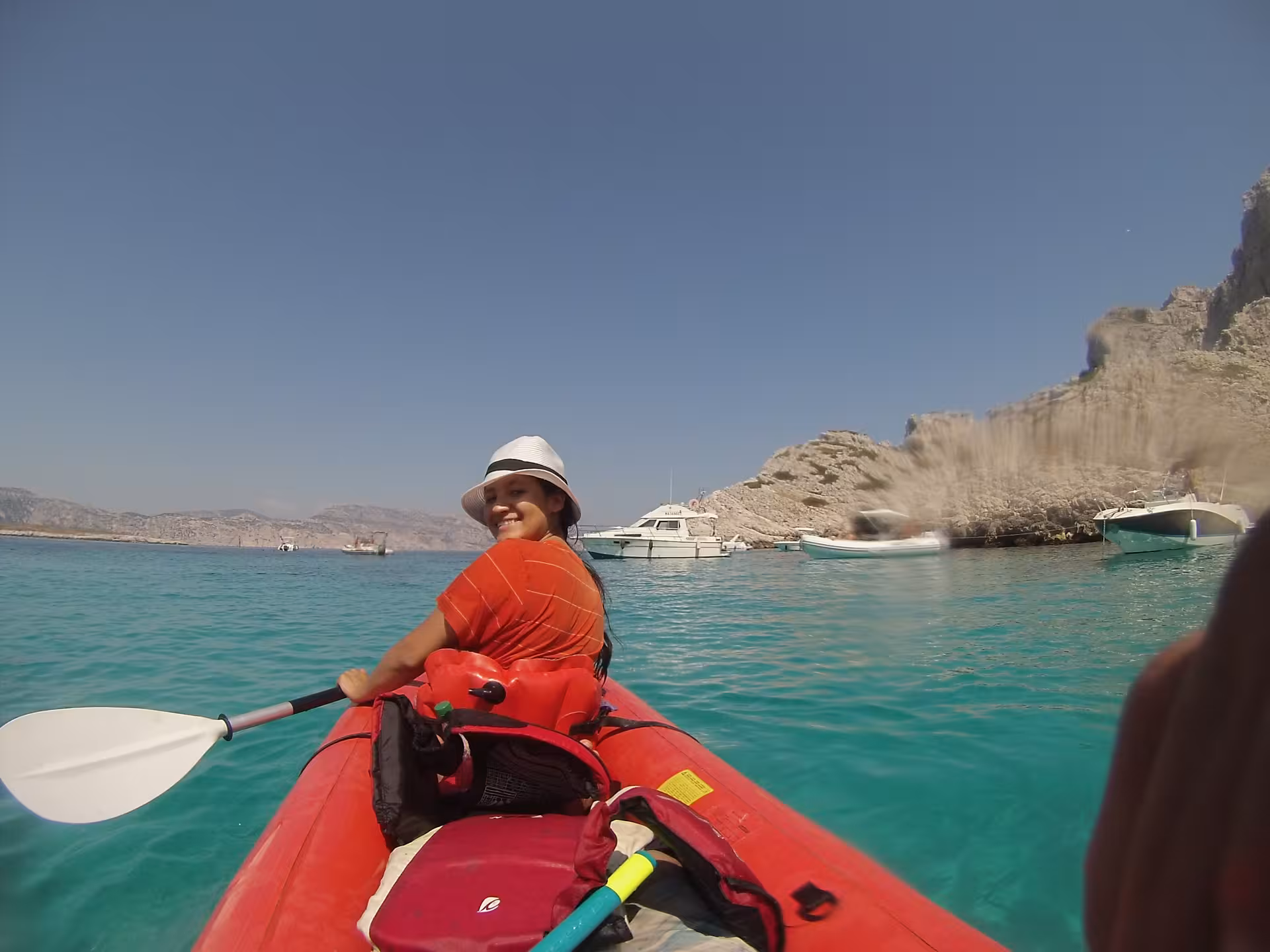 Sea kayak tour to Marseille islands and Calanques, red kayak on crystal-clear water with boats and rocky coast ahead
