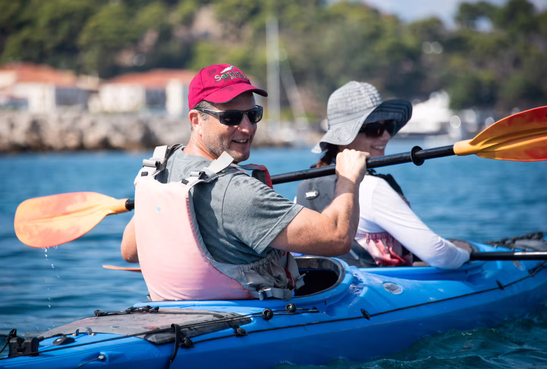 Couple paddling sea kayaks on Navarino Bay near Pylos, Greece, wearing life vests on a guided coastal tour