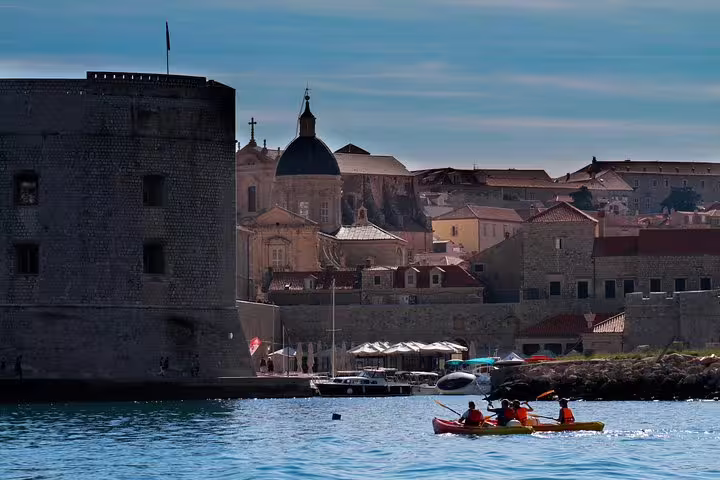 Sea kayakers paddling in a historic old town harbor, combining coastal kayaking and snorkeling day trip