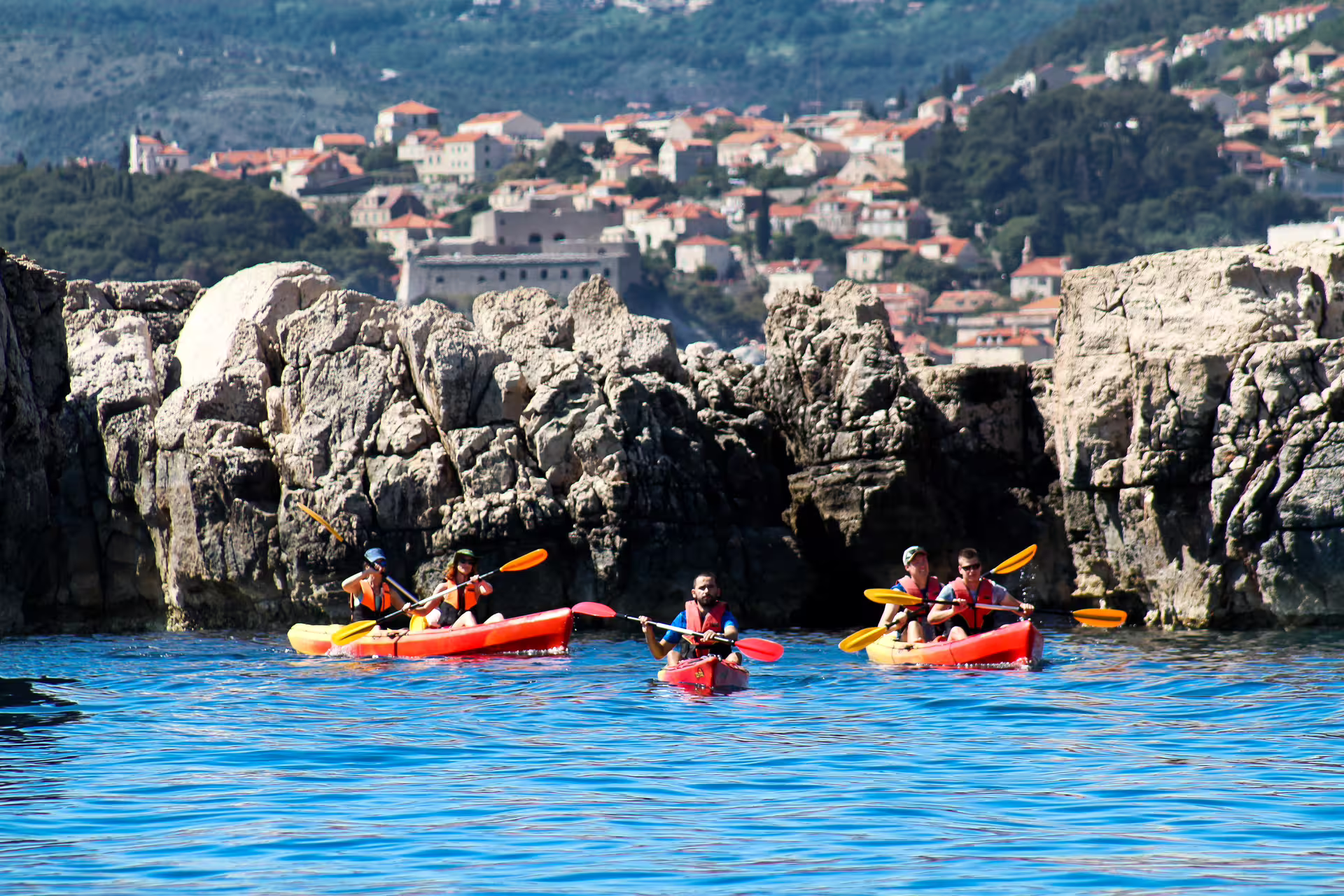 Guided sea kayaking tour along rocky cliffs, paddling in calm blue water with coastal village views
