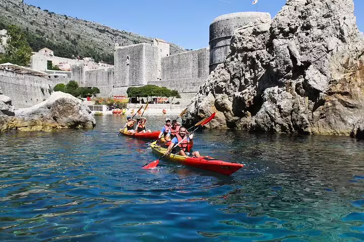 Group sea kayaking near historic coastal fortress and cliffs, guided adventure with snorkeling breaks in clear water