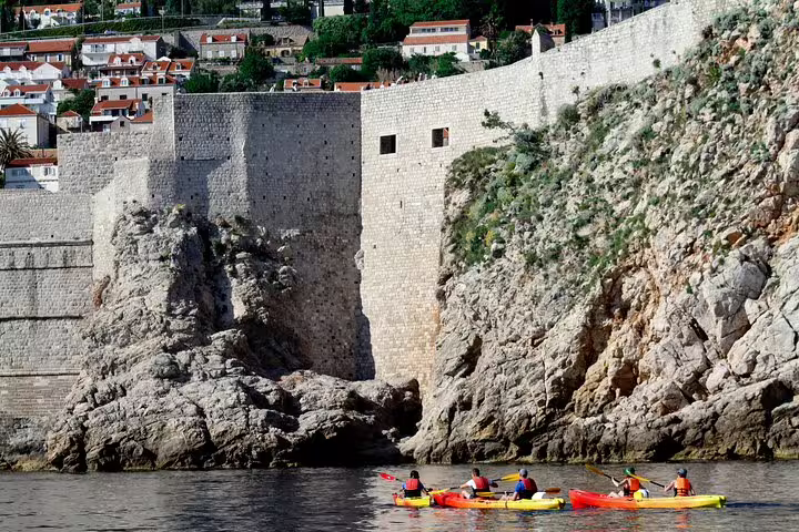 Guided sea kayaking past Dubrovnik Old Town walls, paddling along rocky coast on Adriatic snorkeling tour