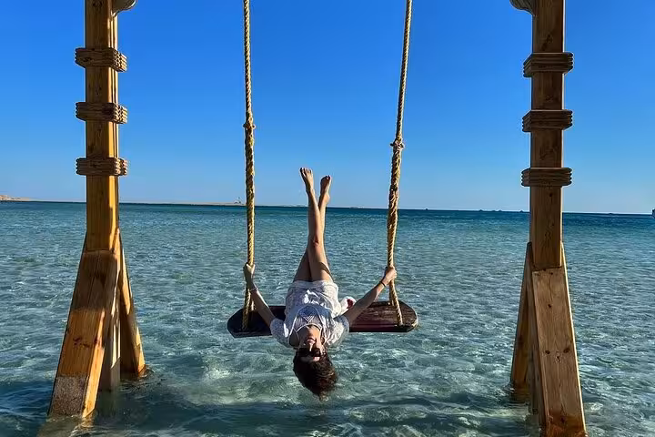 Traveler relaxing on sea swing in shallow turquoise water at Giftun Island, Hurghada boat trip with lunch and water sports