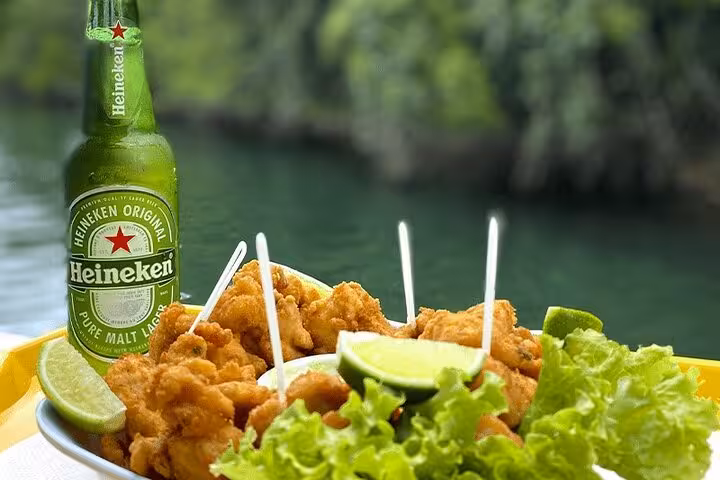Crispy fried seafood dish with lime and a Heineken beer on a boat tour in Paraty, Brazil, against a lush backdrop.