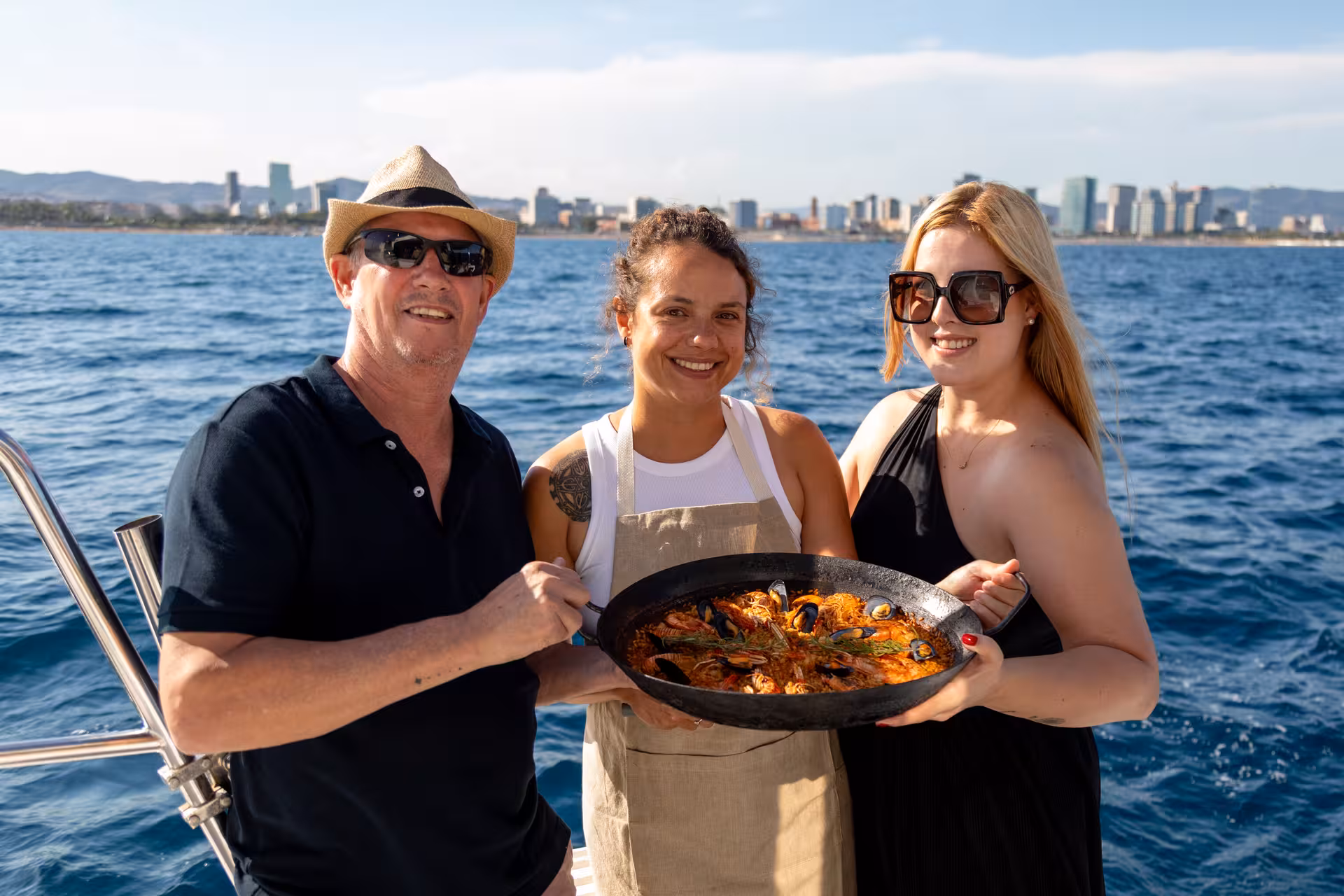 Guests holding a seafood paella pan on a boat, paella masterclass experience with Barcelona skyline views