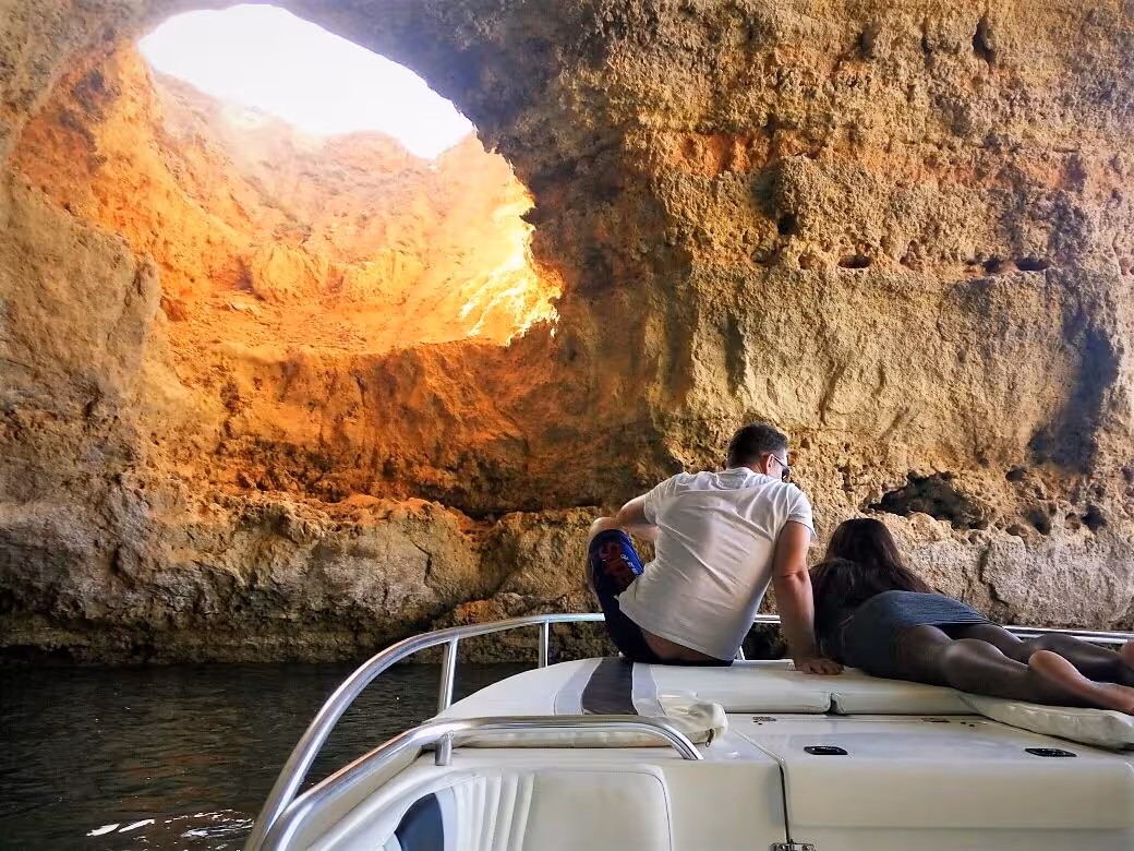Couple relaxing on Seasiren Private Tour 2H boat while admiring sunlight streaming through Benagil Cave’s rocky dome