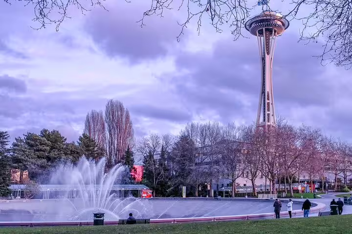 Space Needle tower rising above International Fountain at Seattle Center during dusk with purple sky