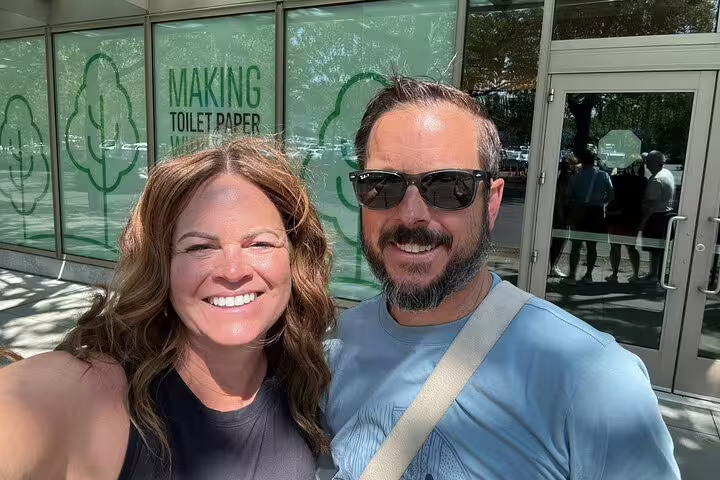 Smiling couple taking selfie outside Seattle building with green toilet paper making signage