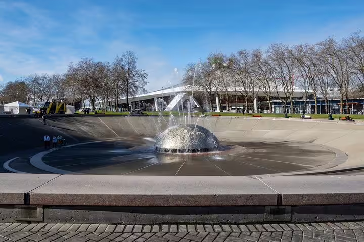 Round fountain with dome water feature in Seattle public plaza with trees and pavilion in background