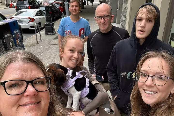 Group of five people with a small dog in a purple harness taking a selfie on a Seattle sidewalk