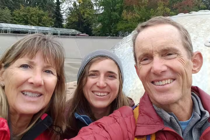 Three smiling adults on a Seattle walking tour posing for a selfie outdoors near a modern silver structure