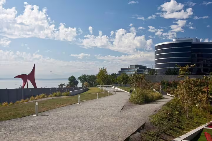 Seattle waterfront walking path with red sculpture and modern circular building on a sunny day