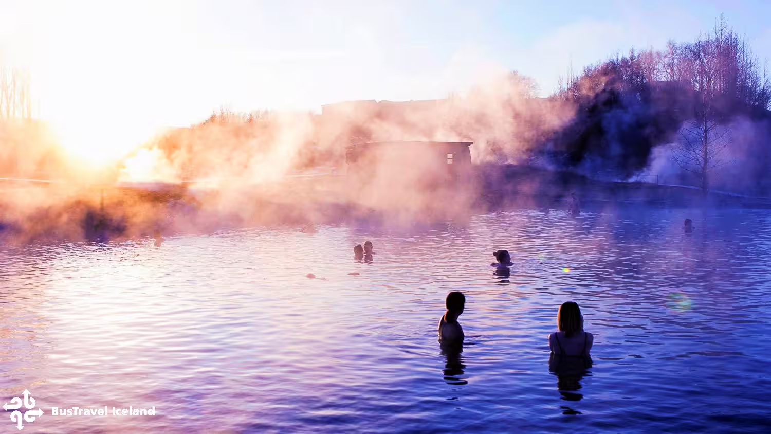 Bathers soaking in steaming geothermal Secret Lagoon hot spring at golden sunset in Iceland