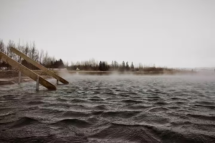 Steaming geothermal Secret Lagoon hot spring with wooden steps and misty water on overcast day