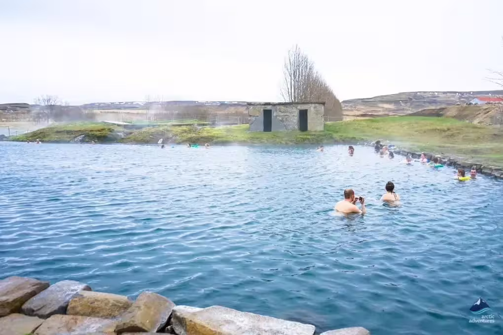 Visitors bathing in the geothermal Secret Lagoon hot spring pool in Iceland with steam rising