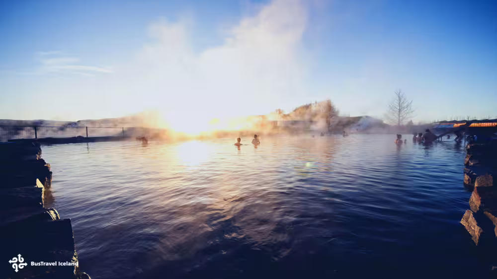 Bathers relaxing in the steaming Secret Lagoon geothermal pool at golden hour in Iceland