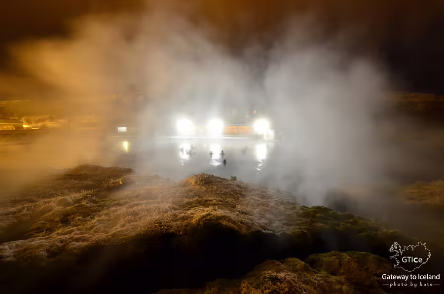 Steam rising over Secret Lagoon geothermal pool at night with bathers silhouetted in glowing water