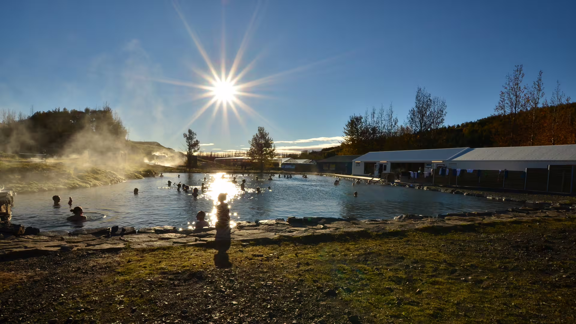 Steaming Secret Lagoon geothermal pool with bathers on a sunny day in Iceland
