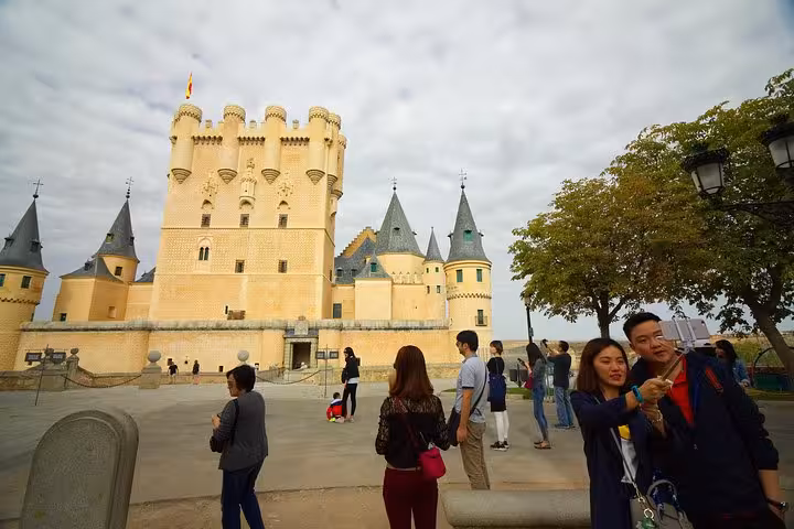 Tourists exploring the majestic Alcazar of Segovia, capturing memories at this iconic castle during a day trip from Madrid.