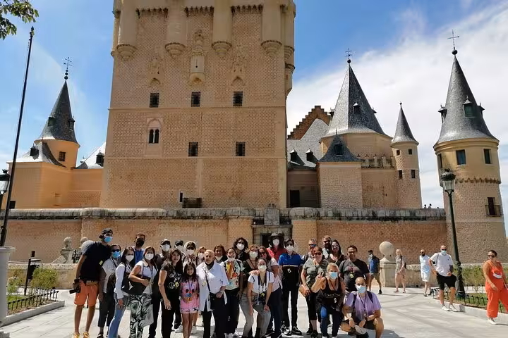 Tour group posing in front of the historic Alcazar of Segovia castle during a guided walking day trip