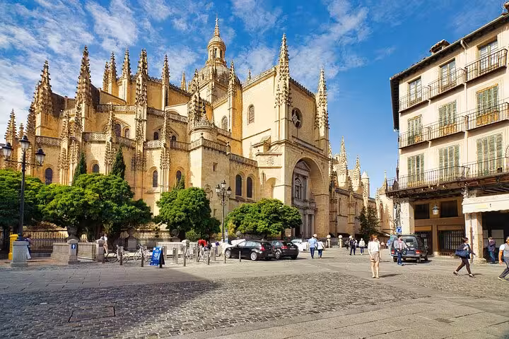 Tourists admire the stunning architecture of Segovia Cathedral under a vibrant blue sky, part of the Segovia and Avila tour.