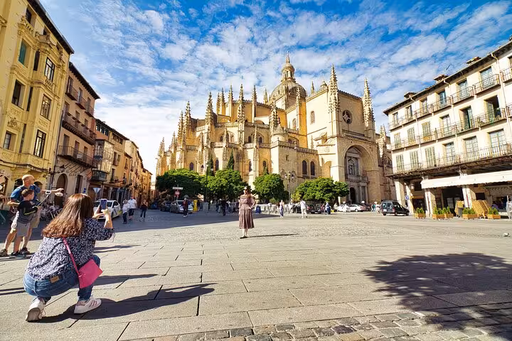 Tourists capture photos of the stunning Segovia Cathedral under a bright blue sky, a highlight of the day trip from Madrid.